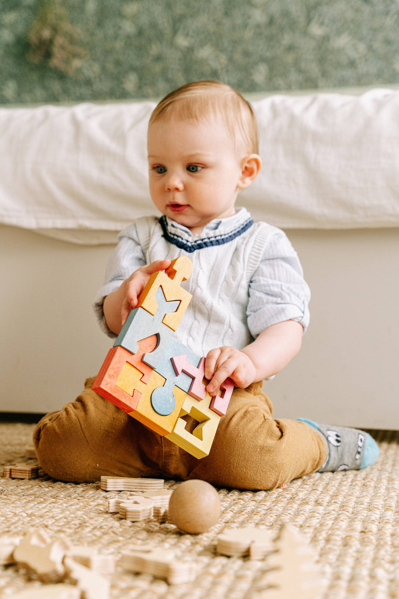 Bébé garçon jouant avec des jouets. Habillé avec un pull en maille blanc, une chemise et jogging camel.